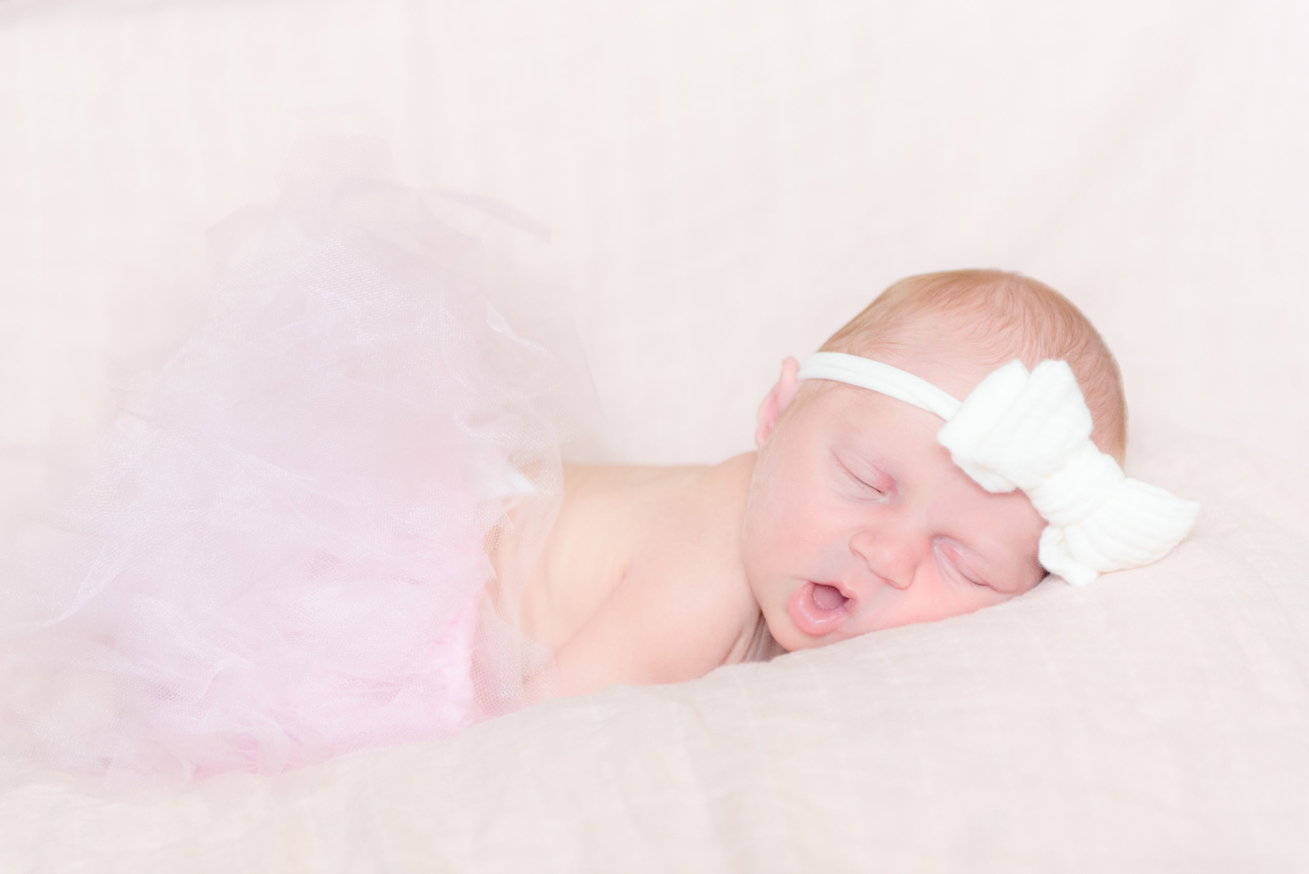 Newborn baby girl wearing a tutu and white bow while sleeping