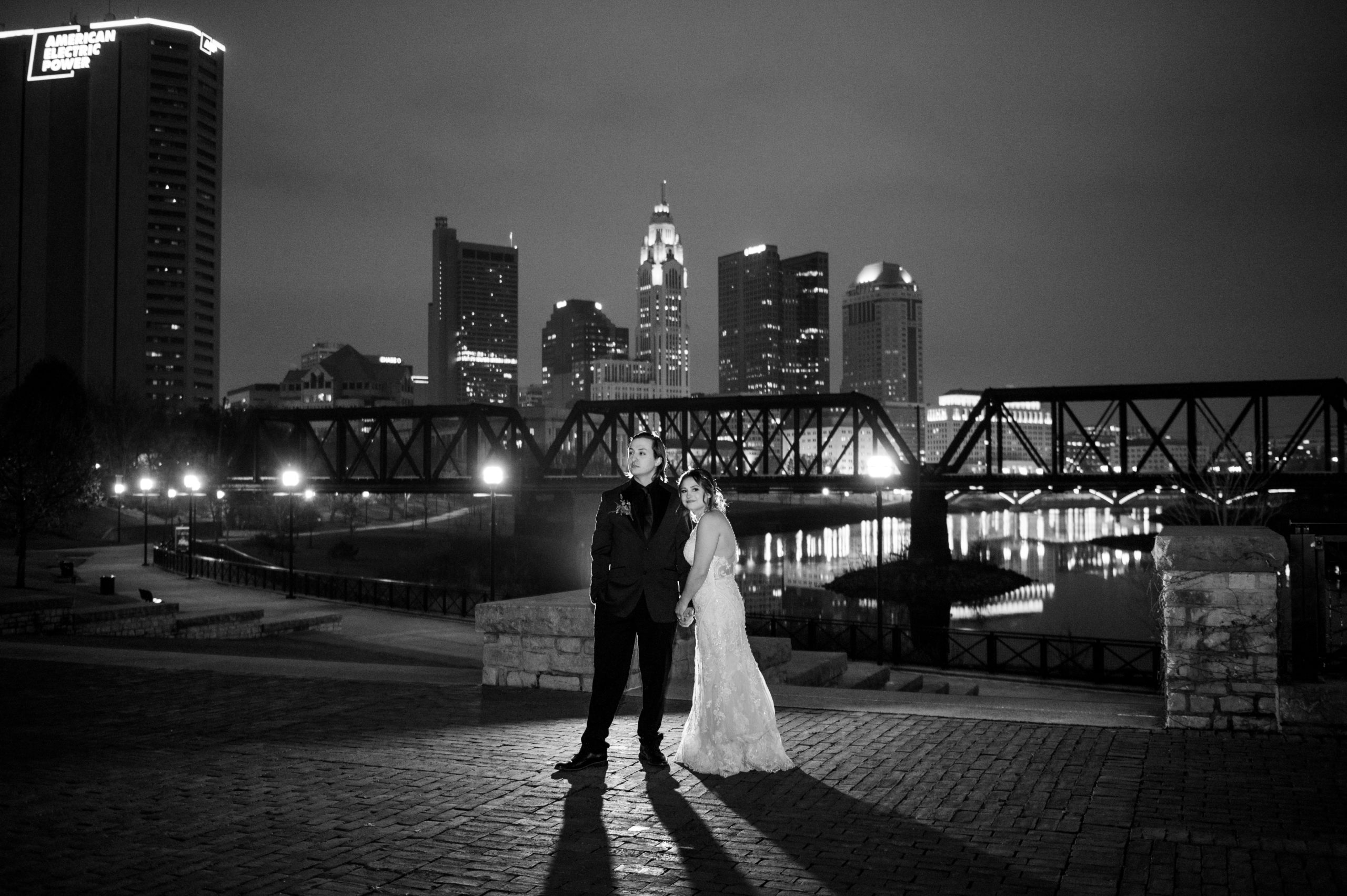 Bride and groom hold hands on the bank of the Olentangy River in Columbus Ohio at night.