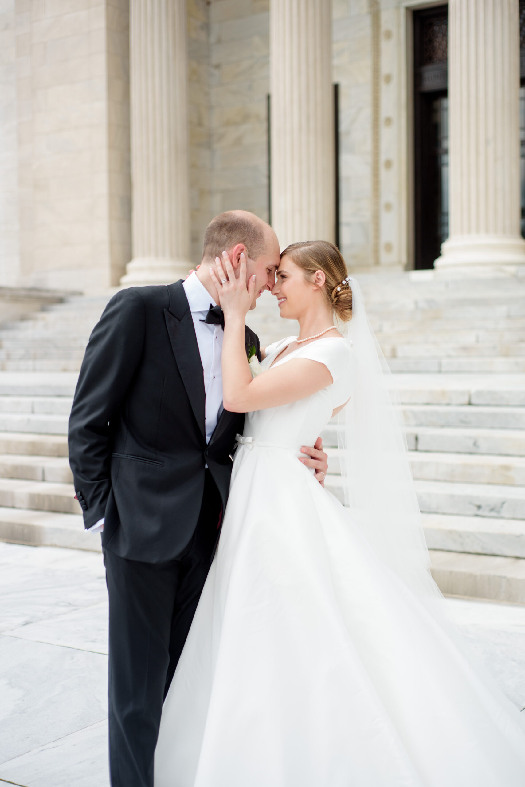 A bride and groom are embracing in front of the stairs at the Cleveland Museum of Art.